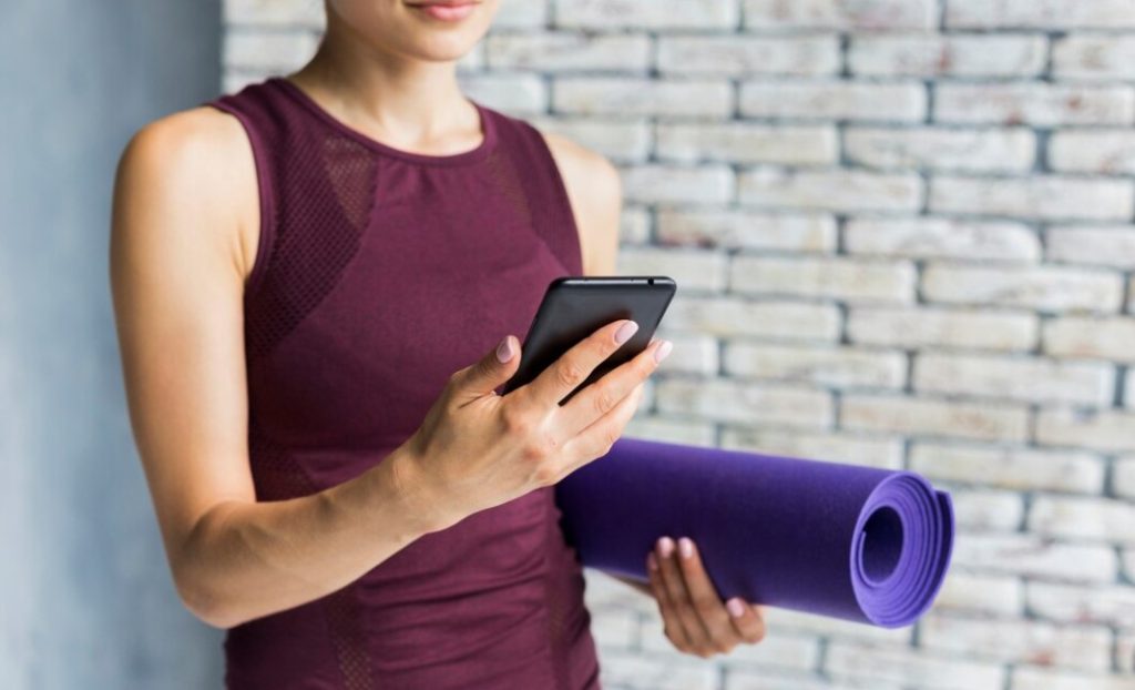 Mulher segurando tapete de Yoga e olhando o celular Mulher segurando tapete de Yoga e olhando o celular